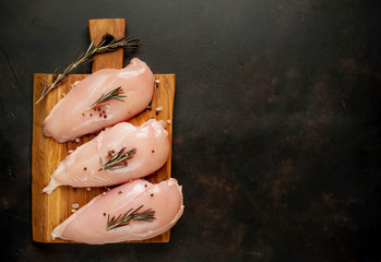 Raw chicken breast fillets, ready for cooking on a wooden cutting board with spices. on a specific background. top view with copy space