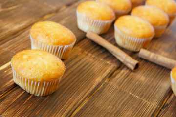 Bright golden cupcakes and cinnamon sticks lie on a wooden surface made of pine boards. Tasty and healthy food. Daylight