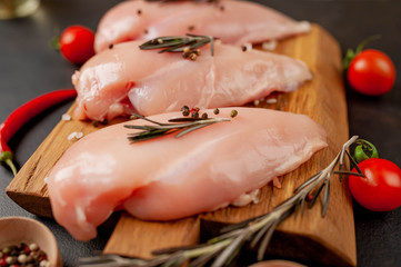 Raw chicken breast fillets, ready for cooking on a wooden cutting board with spices. on a specific background