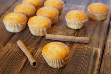Cinnamon sticks and fresh golden muffins lie on the wooden surface of pine planks. Tasty and healthy food