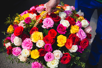 The man works on the delivery of flowers. Carries a large bouquet of multi-colored roses in a wicker basket