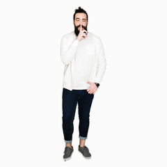 Young man with long hair and beard wearing sporty sweatshirt asking to be quiet with finger on lips. Silence and secret concept.