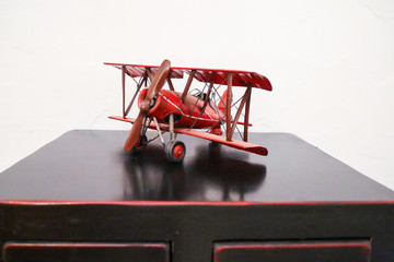 model of a red biplane aircraft with propeller driven engine on a black desk in front of white...