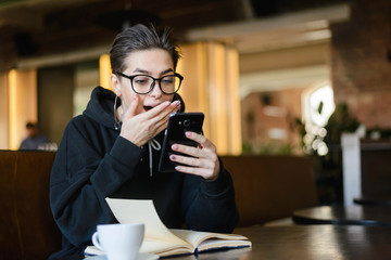 Surprised shortcut hipster young girl getting shocked sms while reading book
