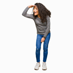 Young beautiful woman with curly hair wearing grey sweater very happy and smiling looking far away...