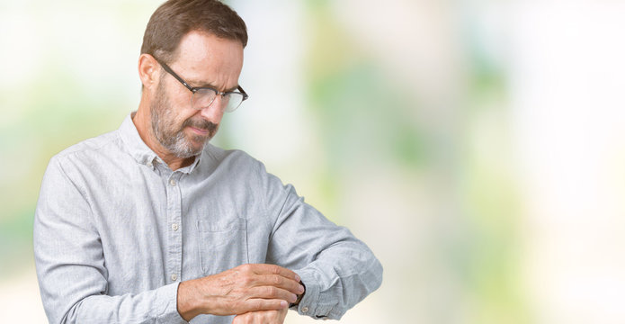 Handsome middle age elegant senior man wearing glasses over isolated background Checking the time on wrist watch, relaxed and confident