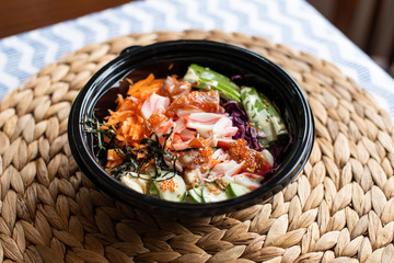 hawaii poke bowl with salmon, rice, surimi, avocado, tobiko, carrot and seaweed