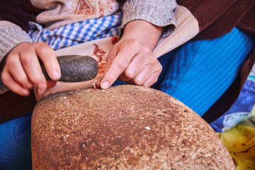 A moroccan woman cracking argan nuts with a stone tool on the stone to produce hand made argan oil for cosmetics and food preparation