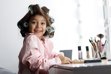 adorable little girl playing with her mother's cosmetic in front of the mirror at home