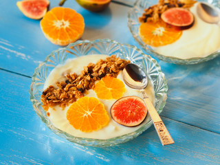 Granola yogurt bowl topping with fresh orange and fig fruit on blue wooden table  for healthy breakfast concept.