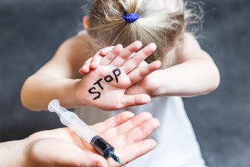 the child covers his face. on hand inscription stop. on the other hand a syringe with a dark...