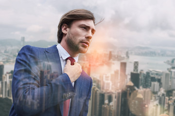 Busy morning. Attractive business expert adjusting his necktie while standing outdoors with cityscape on the background