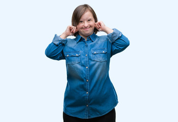 Young adult woman with down syndrome over isolated background covering ears with fingers with annoyed expression for the noise of loud music. Deaf concept.