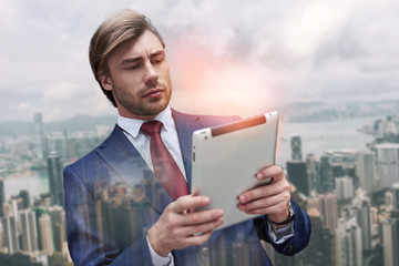 Using modern technologies. Close-up portrait of attractive bearded businessman in suit using digital tablet while standing outdoors