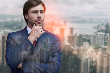 Thinking about business. Handsome bearded businessman touching his chin and looking away while standing against of cityscape background