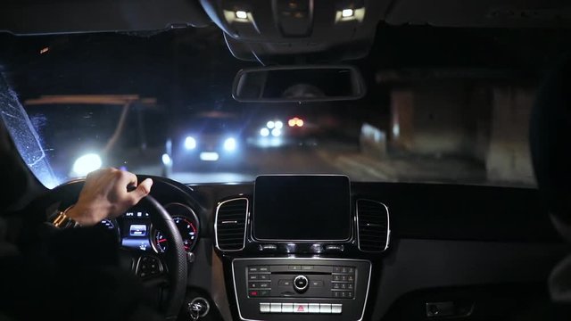 Handsome man driving his car on the city road at night. Back view of the driver and his friend traveling by car.