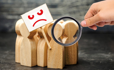 Magnifying glass is looking at an angry mob of wooden figures of people with a sign. Social...