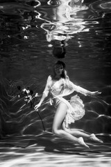 Girl portrait posing underwater in fashion underwear with flowers in hand in swimming pool alone in the deep