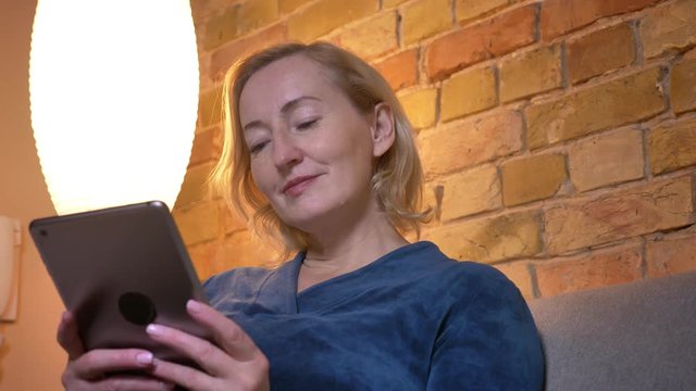 Closeup shoot of eldey caucasian female using the tablet then looking at camera and smiling