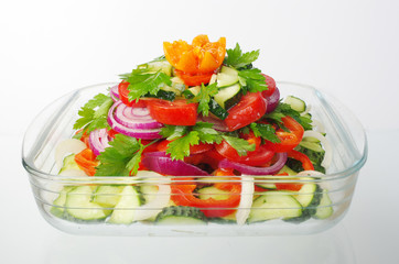Vegetable salad in a salad bowl on white. Tomatoes, cucumbers, onions, garlic, pepper, parsley.