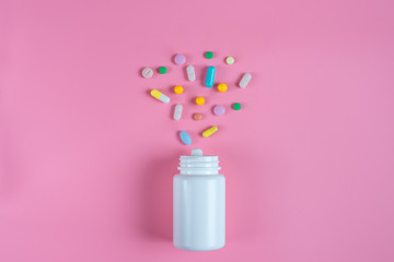 Colored pills, tablets and white bottle on pink background
