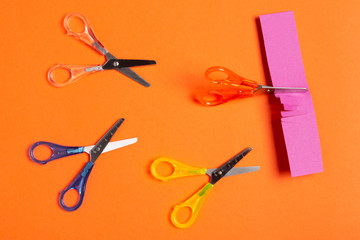 minimal leadership concept, four colored scissors on an orange background, scissors cut paper, business