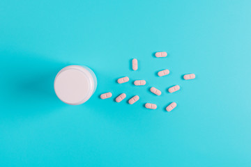 Pink pills, tablets and white bottle on blue background