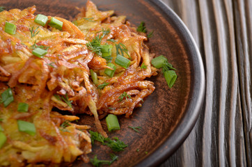 Fresh homemade tasty potato pancakes in clay dish on rustic wooden table