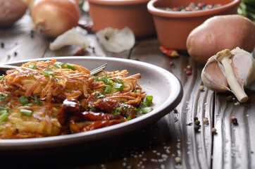 Homemade tasty potato pancakes in clay dish with sun-dried tomatoes and sour cream