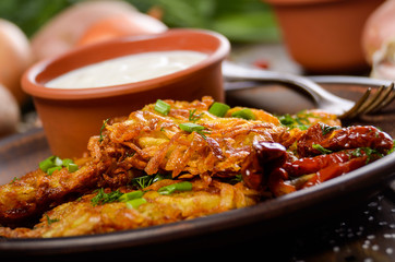 Closeup view at Homemade tasty potato pancakes in clay dish with sun-dried tomatoes and sour creram