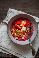 Oatmeal porridge with strawberries and fruit yogurt and pistachios, peanut butter and almond in bowl. Morning concept with copy space