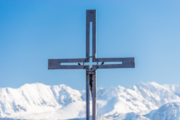 A metal cross visible in the foreground in the background a beautiful view of the Polish Tatra Mountains. Sunny, beautiful day in the winter, snow-capped mountains and blue sky.
