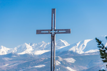A metal cross visible in the foreground in the background a beautiful view of the Polish Tatra Mountains. Sunny, beautiful day in the winter, snow-capped mountains and blue sky.