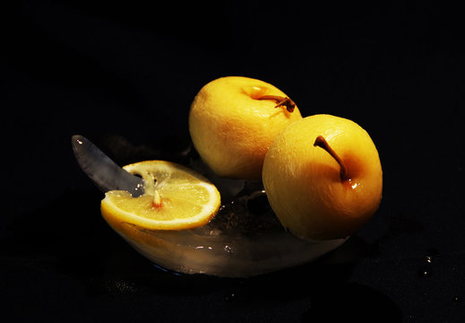 Photo of apples and lemon on the ice in yellow and black colors which can be good illustration of food as fruits and vitamins also as beautiful abstract picture