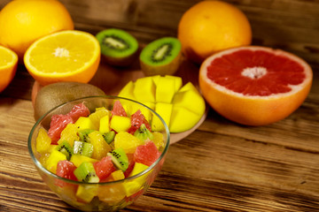 Tasty fruit salad in glass bowl and fresh fruits on the wooden table