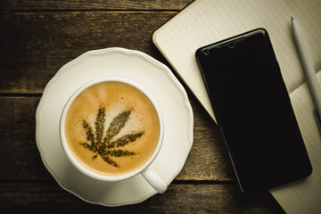 Cannabis coffee - marijuana leaf on coffee foam, rustic wood background