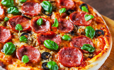 Pepperoni Pizza with Mozzarella cheese, salami, Tomatoes, olive, pepper, Spices and Fresh Basil. Italian pizza on wooden table background