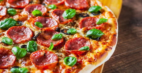 Pepperoni Pizza with Mozzarella cheese, salami, Tomatoes, olive, pepper, Spices and Fresh Basil. Italian pizza on wooden table background