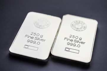 Two minted silver bars weighing 250 grams each on a dark background.