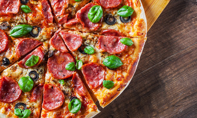Pepperoni Pizza with Mozzarella cheese, salami, Tomatoes, olive, pepper, Spices and Fresh Basil. Italian pizza on wooden table background