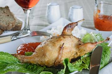Delicious baked quail in a ceramic plate with rice and red sweet and sour sauce next to glass of red vine prepared for a delicious lunch or dinner