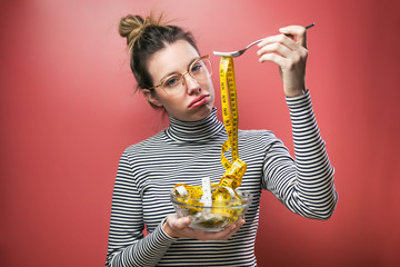 Frustrated beautiful woman with eyeglasses looking at camera while holding bowl with measuring...