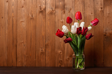 tulip flowers are in a vase, wooden background