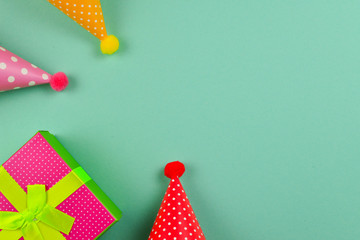 Fototapeta premium Birthday caps and a present, confetti on a green background. Space for text or design.