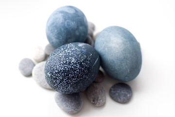 Fototapeta na wymiar Three colored blue, gray marble eggs lie on a white background on stones