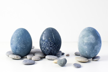 Three colored blue, gray marble eggs stand vertically among the stones