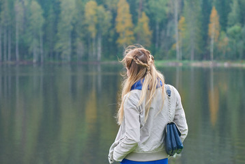 The portrait of a beautiful young woman with long blonde hair on the wooden quay against the forest and lake.