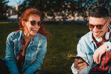 Happy young couple in love using smartphone while sitting in a green park