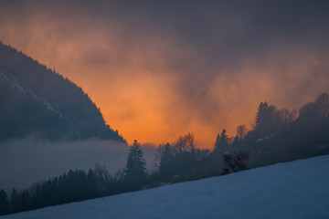 Dramatic sunset on forest near mountain Grimming on foggy evening
