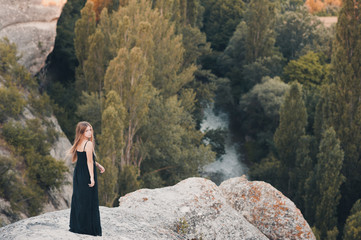 Naklejka na ściany i meble Young girl standing at rock top over beautiful nature view outdoors. Looking at camera.